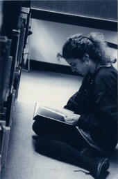 Woman reads in library stacks, circa 1992-1994.